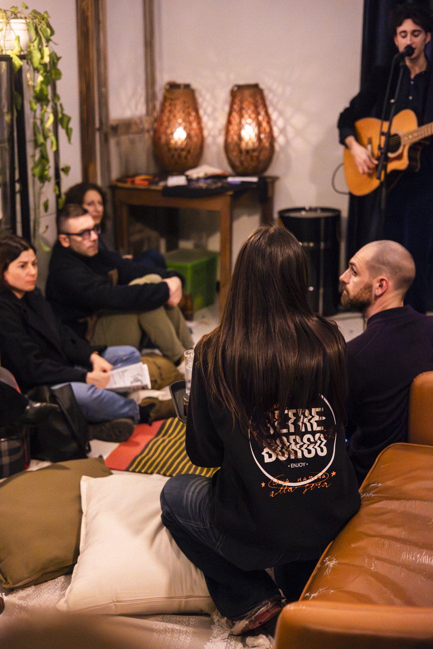 Pubblico seduto su divani e cuscini, artista a pochi passi: atmosfera intima di Velluto Sonoro al Borghetto.